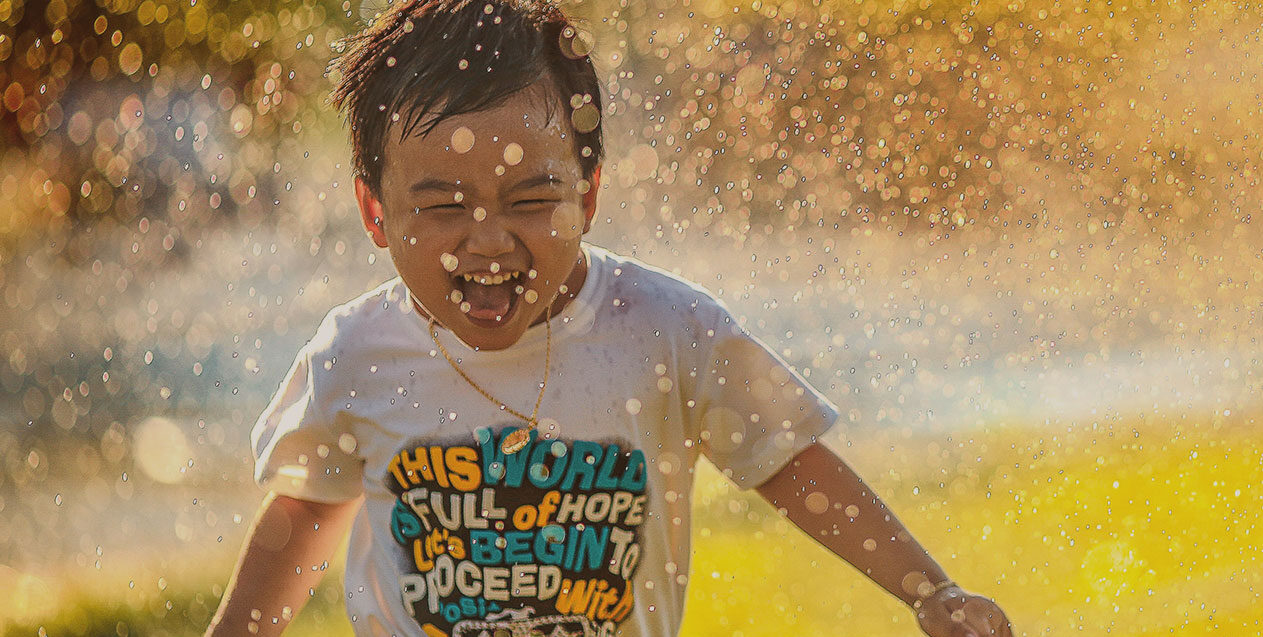 little boy playing in sprinkler