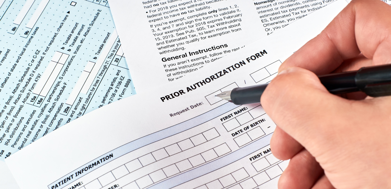 Patient's hand fills out a prior authorization insurance form.