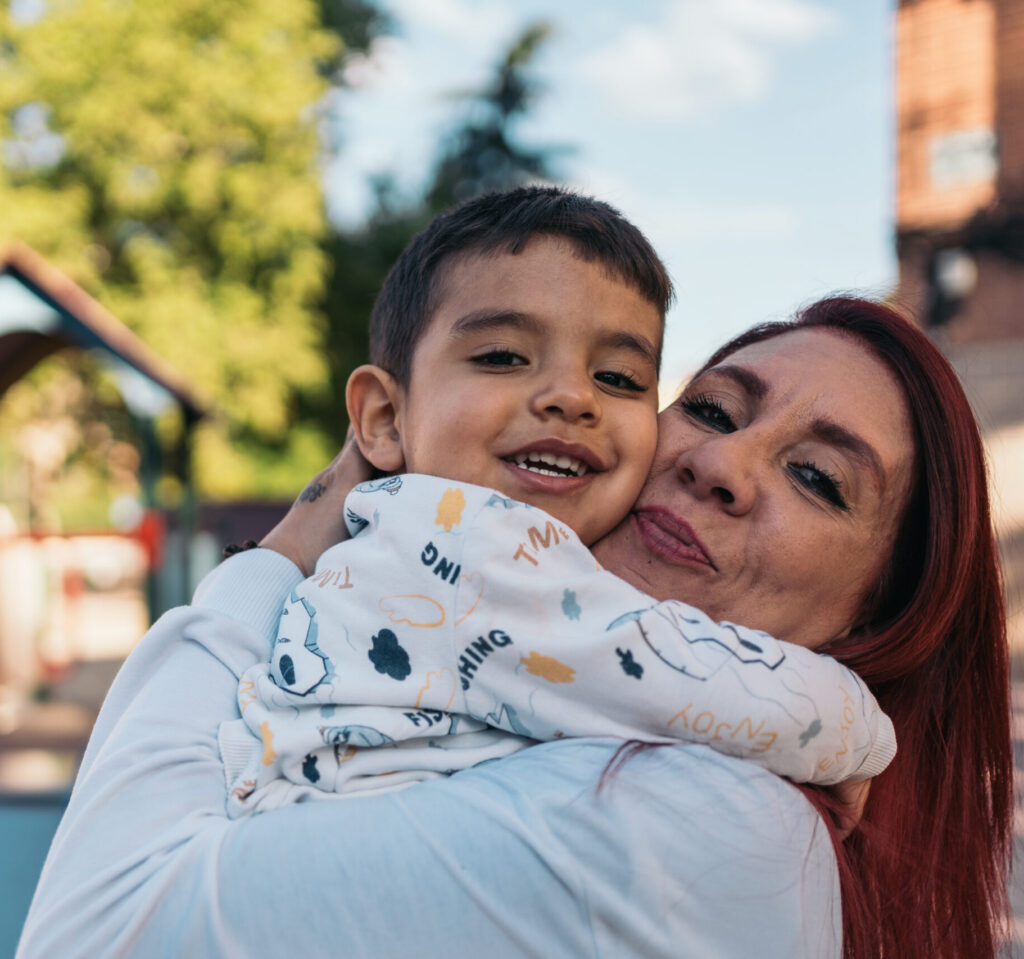 Joyous mother hugs her autistic smiling young son at a sunny playground